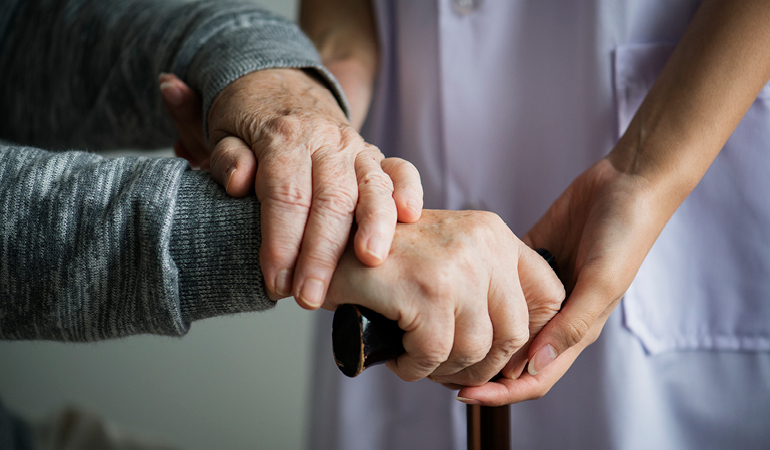 A senior patient receiving gentle physiotherapy to improve gait in a rehabilitation area of a Parkinson care home near Delhi.